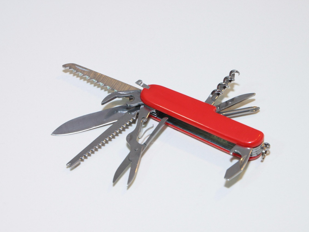 Ein aufgeklapptes Taschenmesser mit rotem Griff, aus dem mehrere Werkzeuge wie Klinge, Säge, Schere und Korkenzieher herausragen.