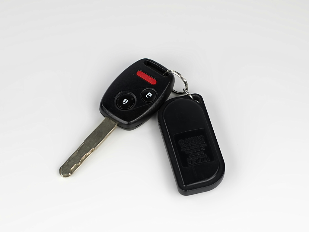 Ein moderner Autoschlüssel mit Fernbedienungsfunktionen und ein zugehöriger schwarzer Anhänger, die an einem Schlüsselring hängen und auf weißem Grund liegen.